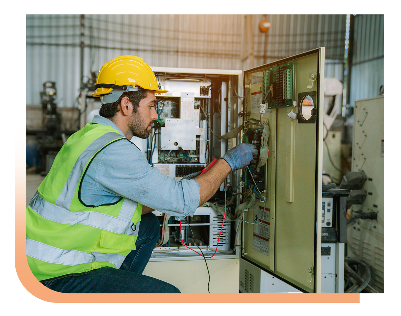 Male technician in a yellow hard hat and neon safety vest inspecting an open industrial control cabinet inside a factory setting.