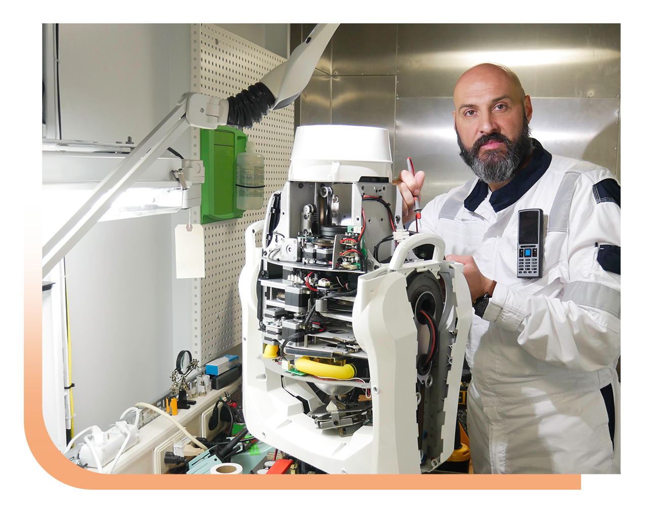 Technician in a white lab coat repairs an exposed robotic device in a lab workspace.