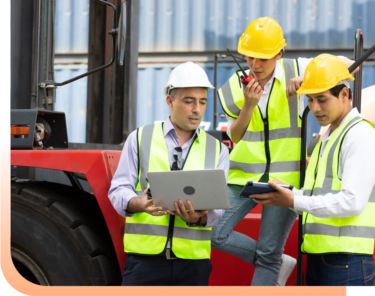 Three construction workers in high-visibility vests and hard hats review plans on a laptop at a busy job site near a red forklift.